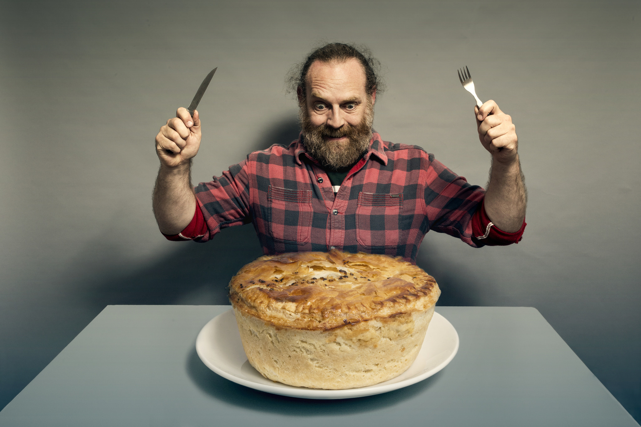 man-sitting-on-a-chair-with-holding-cutlery-fork-and-knife-on-hand-in-front-of-the-giant-drama-pie.jpg